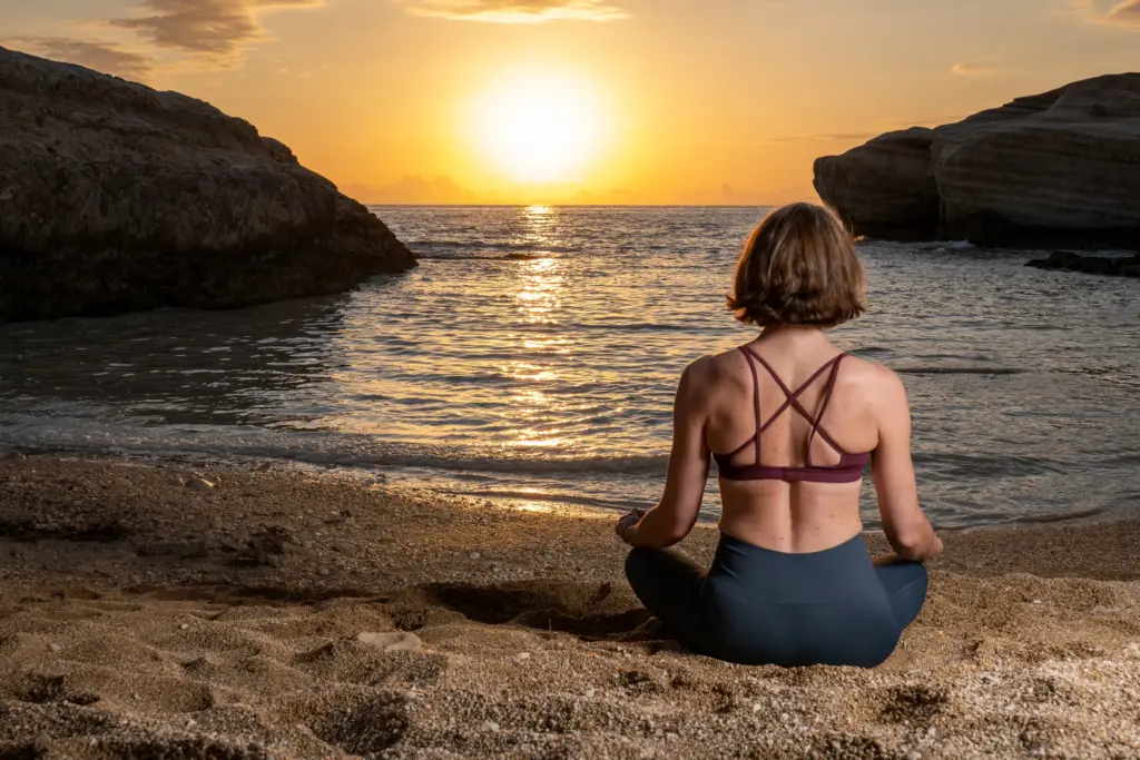 Woman meditating on a Cyprus beach at sunrise with the sun reflected on the sea